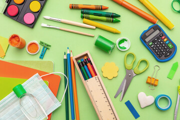 Coronavirus spread prevention measure at school. Surgical mask, alcohol disinfection gel and stationery on pastel green background,