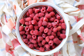 Ripe red garden raspberries in a round plate, on a colored cloth.
