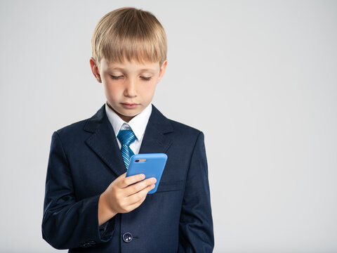 Photo of a  businessman  boy with smartphone .  White  kid in a blue business suit holding a cell phone. 8 years old child dressed in a business formal suit with tie looking on smart phone.