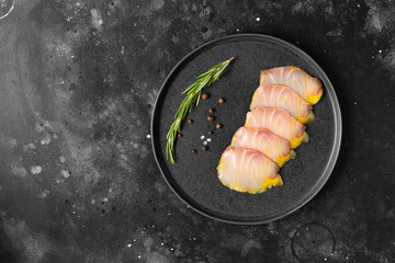 Cold-smoked sturgeon. Slices of sturgeon fish in a black ceramic plate on a black kitchen table....