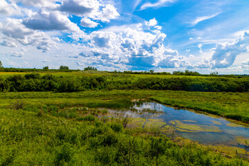 Fototapeta na wymiar A beautiful wide angle view of a pond hidden at the bottom of a lush valley near Saskatoon Saskatchewan, Canada 