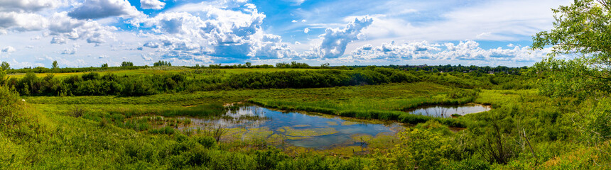 Obraz na płótnie Canvas A beautiful panoramic view of a pond hidden at the bottom of a lush valley near Saskatoon Saskatchewan, Canada 