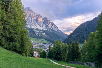 A path leading through an alpine meadow to the village of Corvara at the foot of the Dolomites in Italy