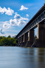 a view of the train bridge in the City of Saskatoon from below on the shore of the South Saskatchewan River. a long exposure time was used to smoothen the surface of the water in the river