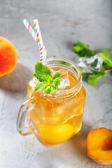 Mug of Peach ice tea on concrete gray background with mint and ice