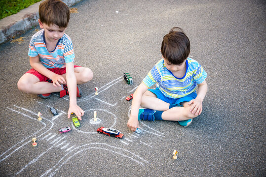 Two brothers sibling kid boy having fun with picture drawing traffic car with chalks. Creative leisure for children outdoors in summer. Difficult traffic rules education friendship concept