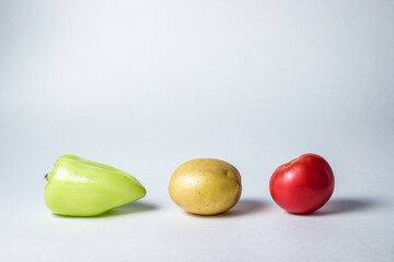 Three vegetables lie on a white plate. The pepper, tomato and potato are next to each other.