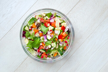 Fresh and healthy vegetables for salad in a glass bowl placed on white wooden surface.
