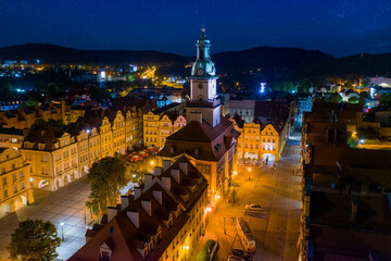 Starry evening over Jelenia Gora market square in Lower Silesia, Poland. Beautiful illuminated town hall building, old tenement houses and restaurants around central place. Mountains in a distance