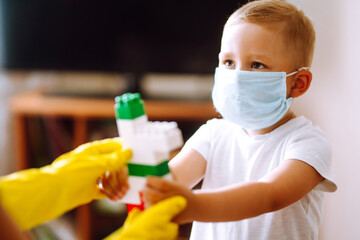 Fototapeta na wymiar Little boy in sterile medical mask plays constructor at home with man in protective hazmat suit during pandemic. Covid-2019. 