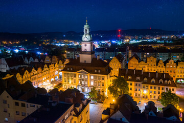 Beautiful illuminated town hall building in Jelenia Gora, Poland surrounded by tenement houses, restaurants and Karkonosze mountains. Evening at market square under starry night. Winter destination