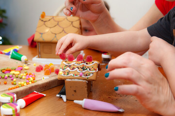 Decorating home baked gingerbread houses with colorful sweet pastilles and sparkling glitter.