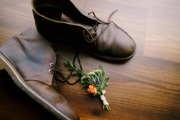 The groom's bud and men's brown leather shoes are on a wooden texture.