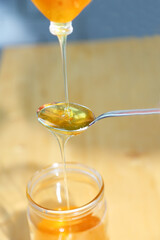 Drops and flows honey on a spoon. Bee honey flows from a spoon into a glass jar. Near. Concept: Natural, healthy and sweet food. Healthy diet.