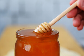 A person's hand holds a honey spoon. Dips a ladle into a jar of honey. Glass jar filled with bee honey. Close-up view. Sweet food.