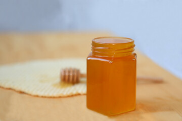 A jar filled with honey stands on a wooden table. In the background is a wooden spoon for med on the cake. Cooking. Delicious food. Preparing a sweet dish of bee honey.
