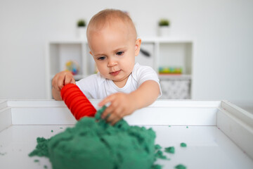 Baby playing with green kinetic sand and rolling pin. Little girl playing with sand at home, games, education, children room