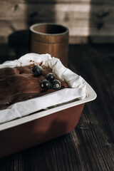 
brownie cake garnished with frozen blackcurrant berries in a brown mold with white parchment on a dark background