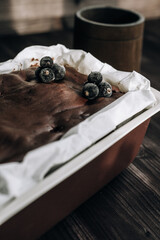 
brownie cake garnished with frozen blackcurrant berries in a brown mold with white parchment on a dark background
