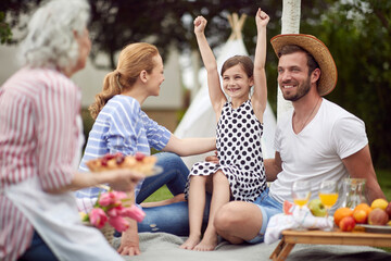 happy little girl with her hands up, sitting in dad's lap, surrounded by family