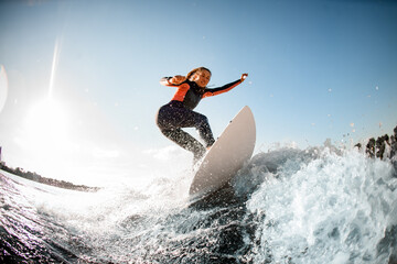Athletic young woman in wetsuit stands on surfboard and rides on the wave. - obrazy, fototapety, plakaty
