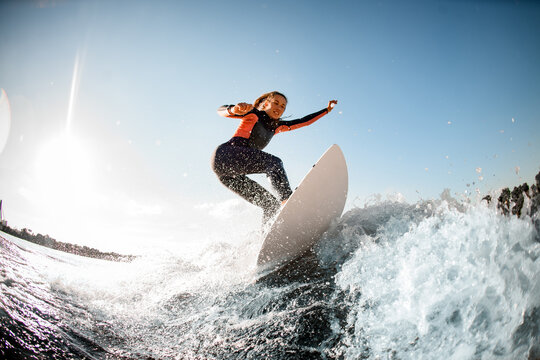 Athletic young woman in wetsuit stands on surfboard and rides on the wave.