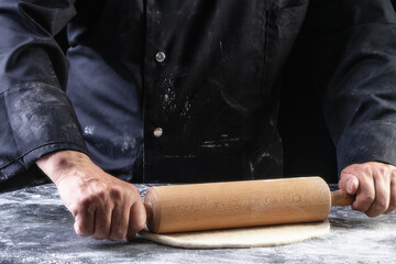 Chef keep rolling pin with dough on dark table, top view
