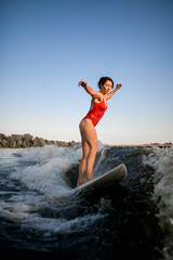 woman in red swimsuit balanced on surfboard and rides on the wave.
