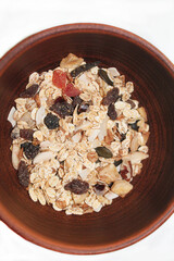 A deep brown clay plate with muesli on a white background, top view, close-up. Cereals with a variety of nuts, pieces of fruit and seeds. Healthy food. Breakfast.