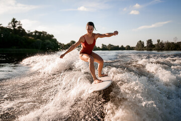 Fototapeta premium handsome woman rides down on surfboard on river wave from boat