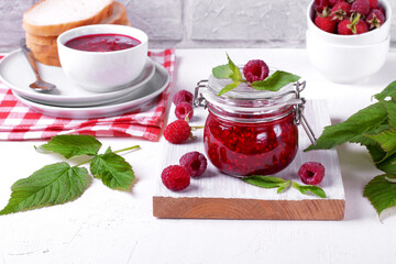 Raspberry jam in glass jar on the white table