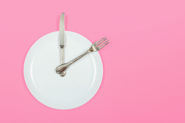 Time to lunch, plate as a clock shows two o'clock in the afternoon on a pink background