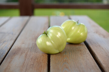 Green tomatoes lie on a wooden table. Two green tomatoes. Unripe tomatoes on a wooden background.
