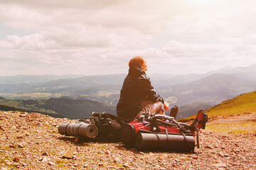 Young blonde woman tourist resting on a hiking backpack in the mountains