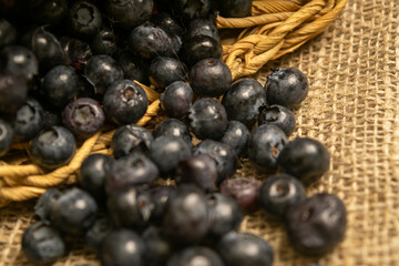 Blueberries in a wicker basket and blueberries scattered on a background of homespun fabric with a rough texture. Close up.