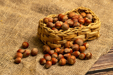 Hazelnuts in a wicker basket and hazelnuts scattered on a background of homespun fabric with a rough texture. Close up.
