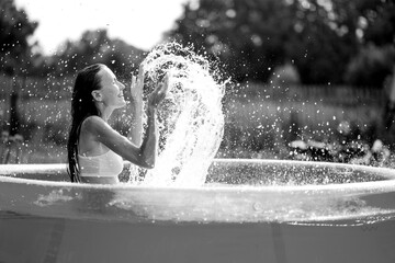 Beautiful woman splashing in inflatable swimming pool outdoor, having fun