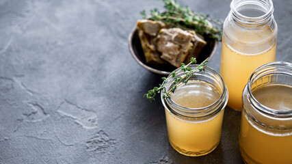 Glass jar with yellow fresh bone broth on dark gray background. Healthy low-calories food is rich...