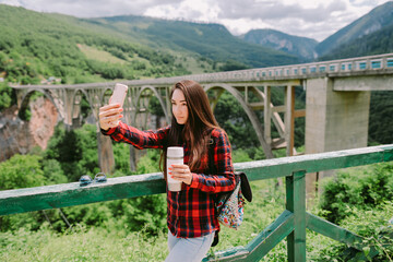 woman travel and taking photos on smartphone at countryside with mountains view. Attractive woman drinks coffee and travel in mountains with beautiful summer view. National park of Durmitor