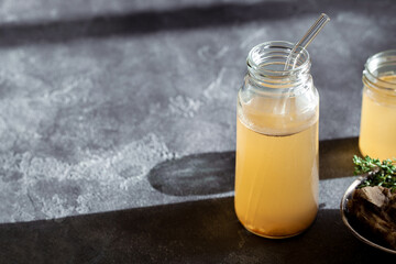 Fresh vegetable bone broth in glass jar with straw on dark gray background. Healthy dieting food are rich in vitamins, collagen and anti-inflammatory amino acids