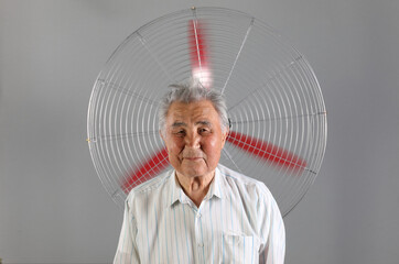 old man struggling with heat and sitting in front of a fan