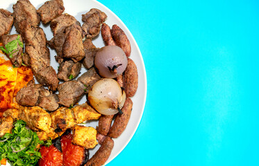 Famous traditional Arabic, Turkish, Israel food. Arabic grilled chicken, lamb, beef, sausages, onion, tomatoes, green, pita bread on white plate on blue background, copy space, top view. Mixed meat