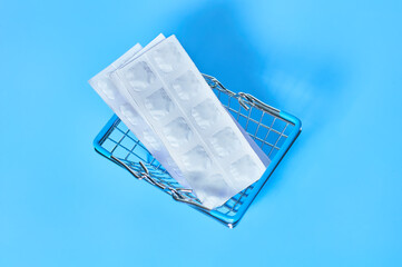 White packaging with pills in market basket on blue background. Purchasing or sell of medicaments. Healthcare concept