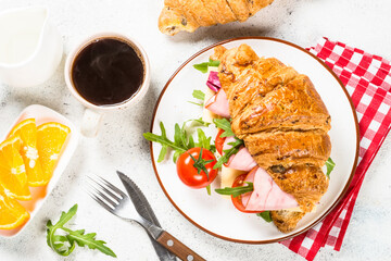 Croissant sandwich with coffee on white table.