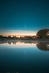 Dobrush, Belarus. Comet Neowise C2020f3 In Night Starry Sky Reflected In Small Lake Waters.