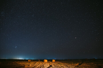 Night Starry Sky Above Haystacks In Summer Agricultural Field. Night Stars Above Rural Landscape With Hay Bales After Harvest. Agricultural Concept