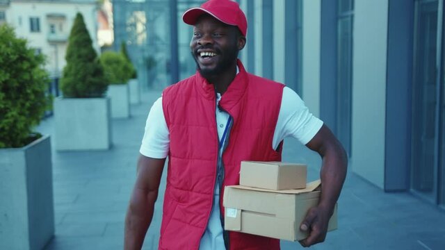 Attractive african american delivery man in uniform walking with a parcel in hands and dancing courier box package worker shipping slow motion