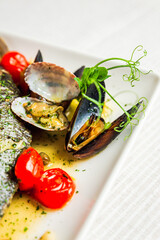 A close-up of mussels and cherry tomatos as a garnish on a white plate