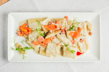 Paccheri pasta with cream sauce and salmon on a white plate