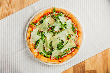 Pizza with arugula or rocket and parmesan cheese on a white plate, top view